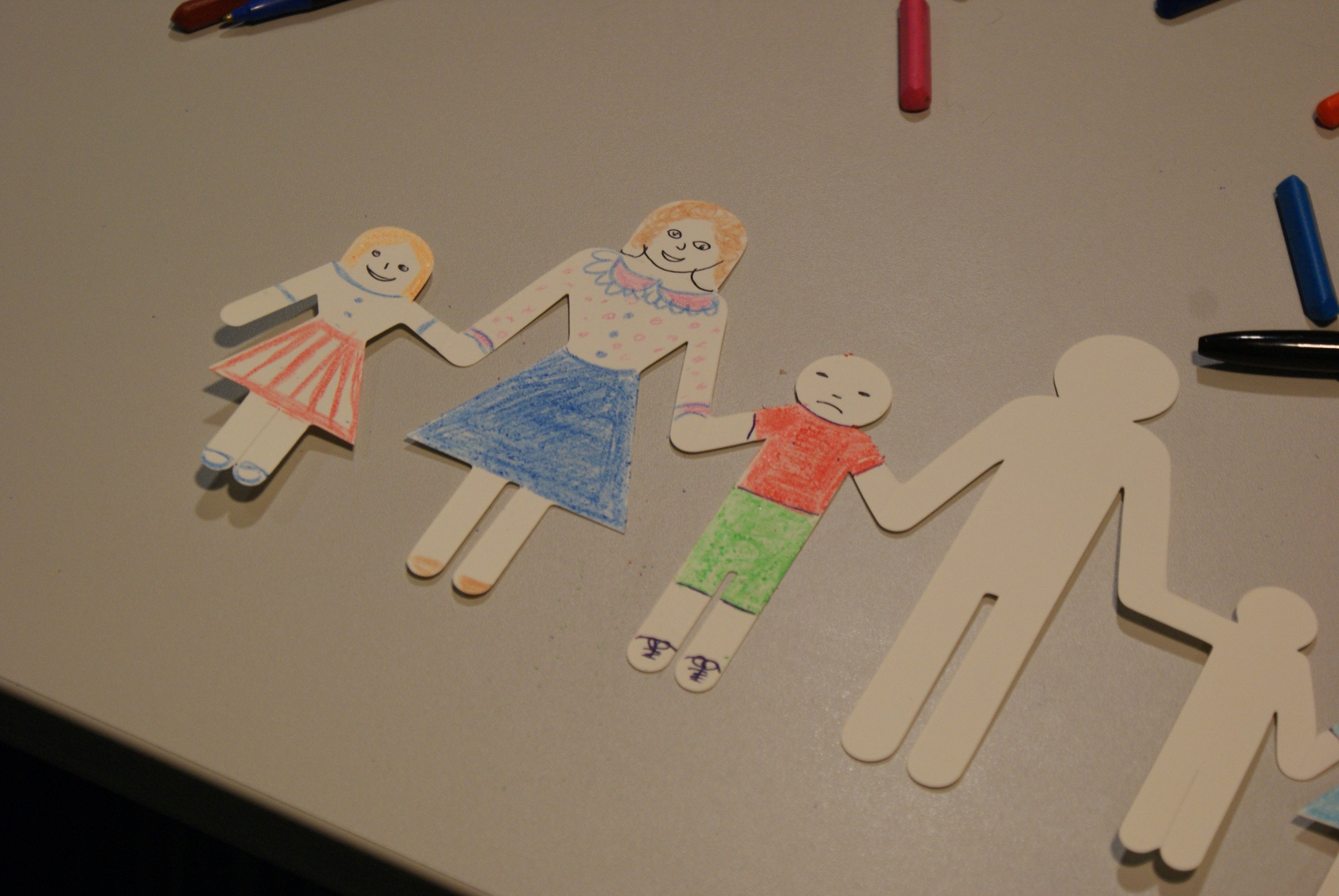 Cut out paper dolls coloured in to show a mother and two children lay on a table.