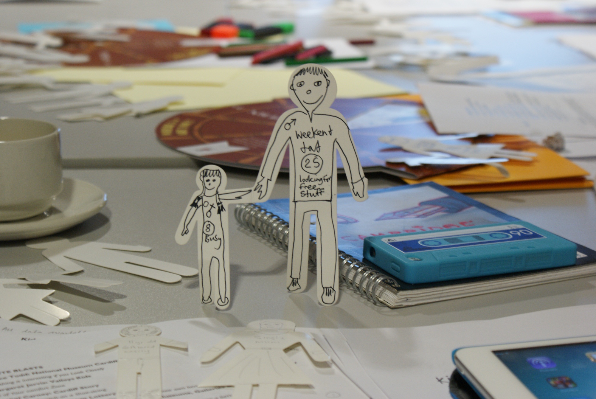 A cardboard cut out of a dad and a child stands on a desk, covered with other workshop materials.