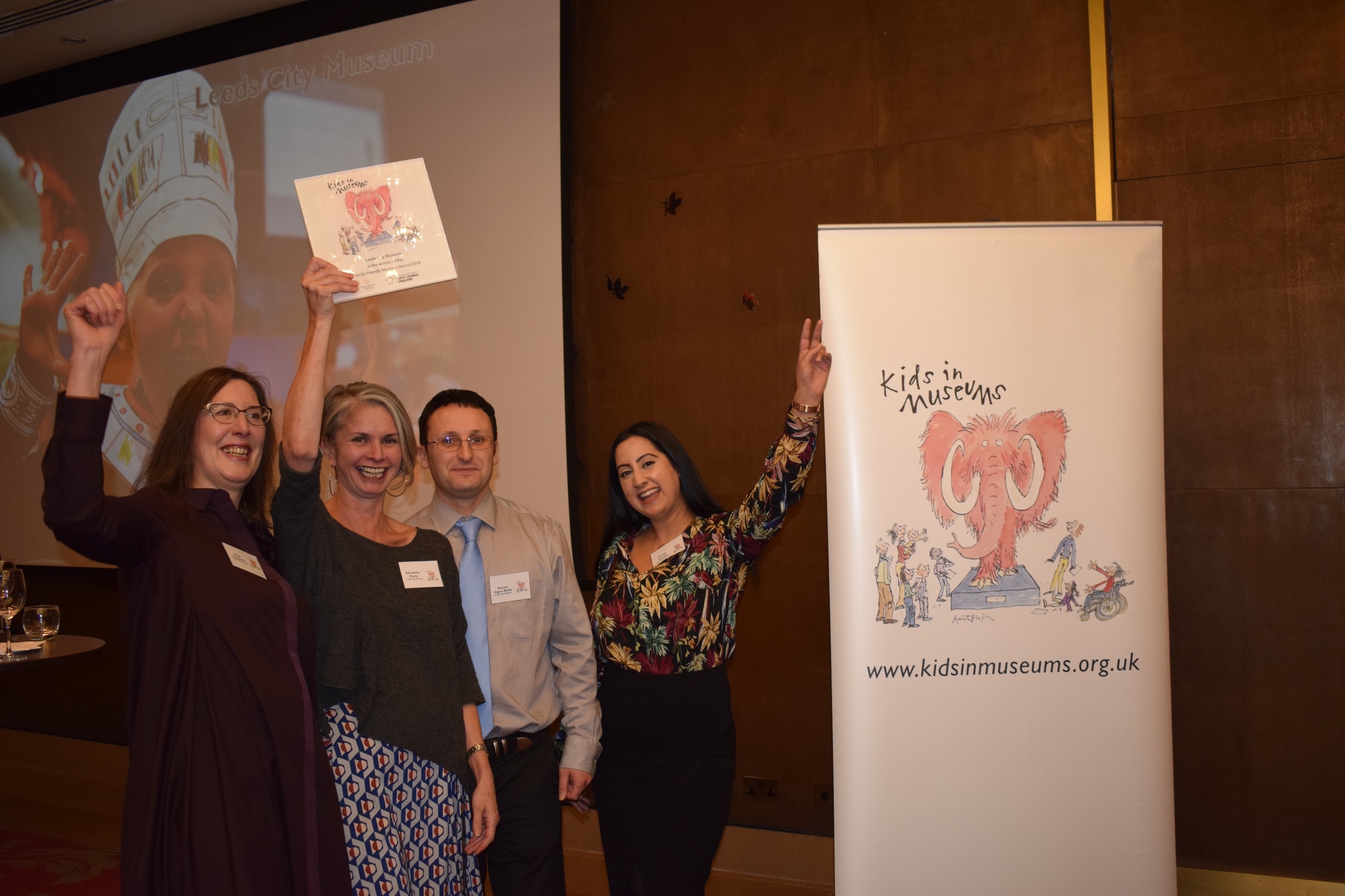 Four members of staff from Leeds City Museum smile and put their hands in the air after winning the Family Friendly Museum Award.