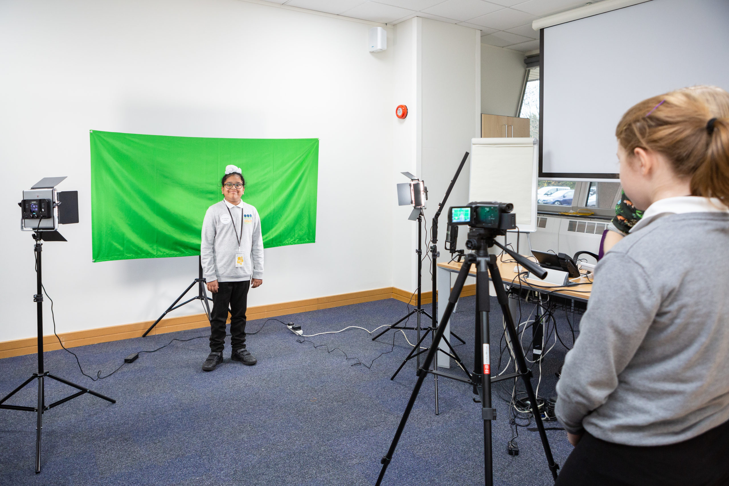 A young girl stands grinning in front of a green screen with camera pointed towards her at the National archives.
