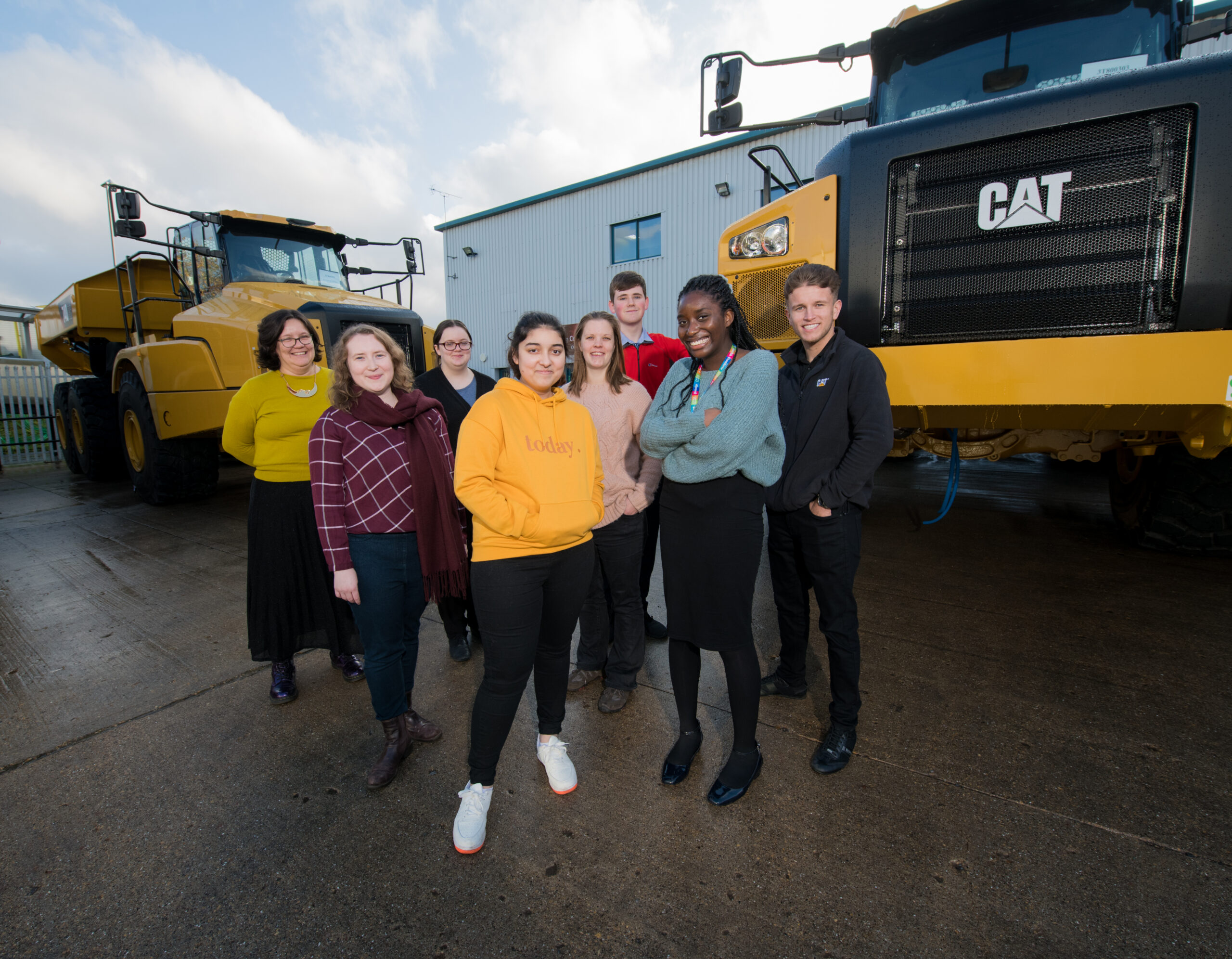 A group of young people standing smiling with a Kids in Museums staff membe in front of Caterpillar vehicles.
