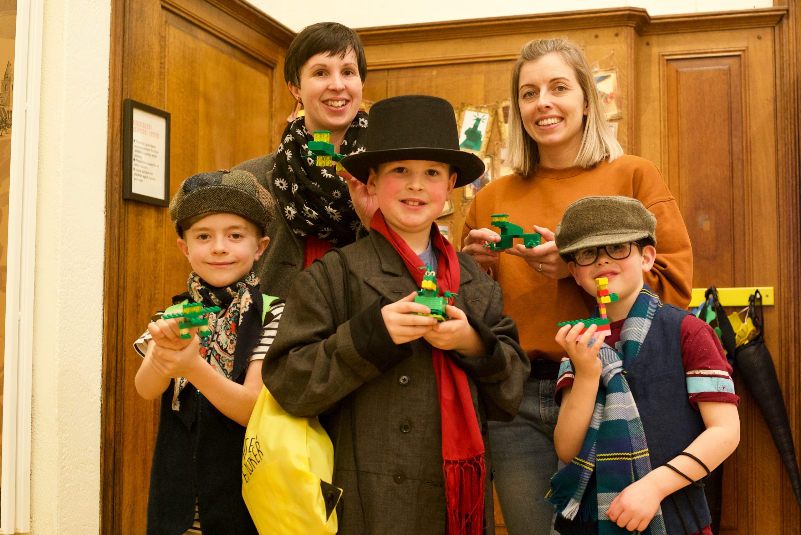 Two mothers and their three boys standing holding the lego dinosausr they designed in the hall at the Andrew Carnegie Birthplace Museum.
