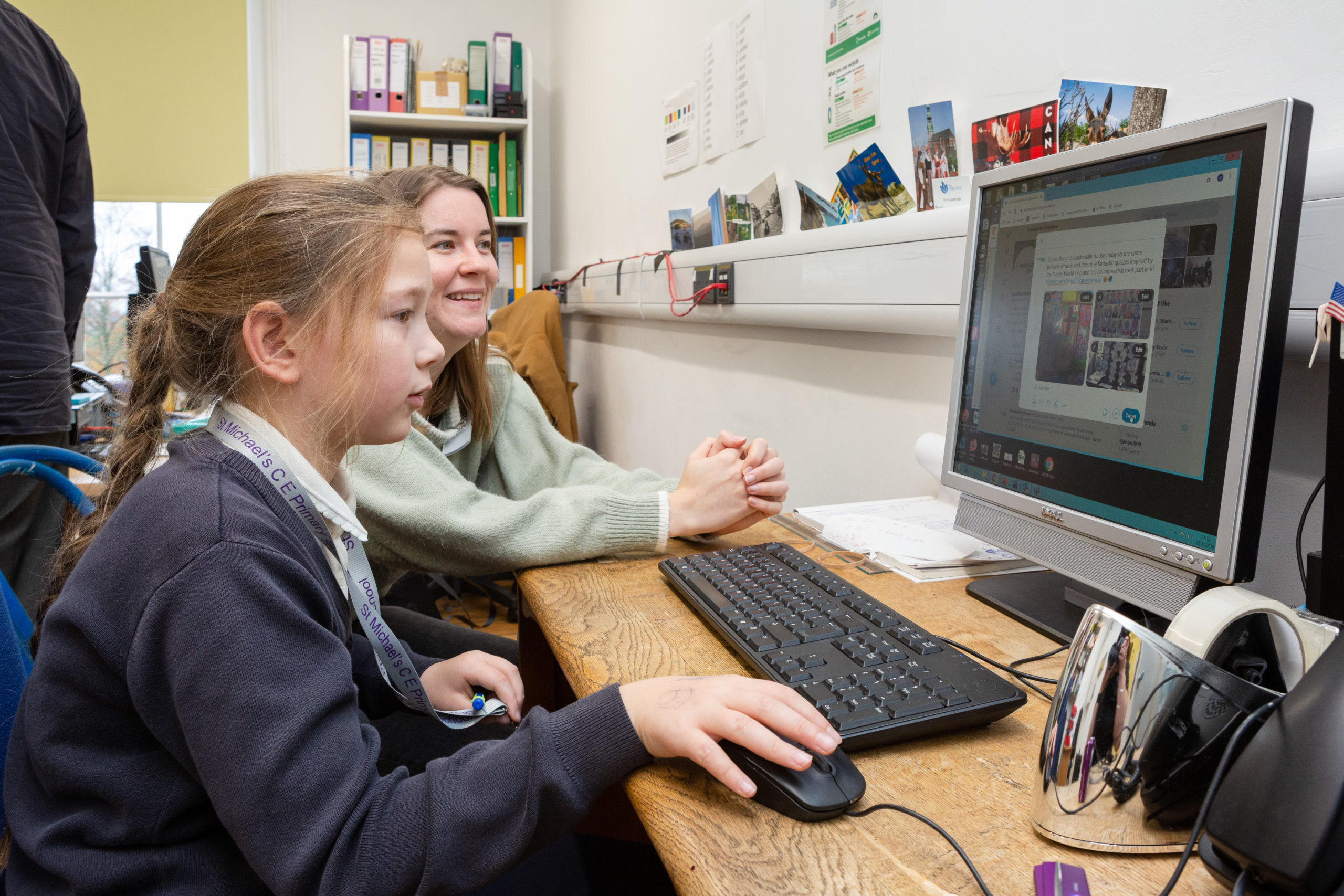 A young girl plays at a computer supervised by an adult sitting next to her in an office at Lauderdale House.