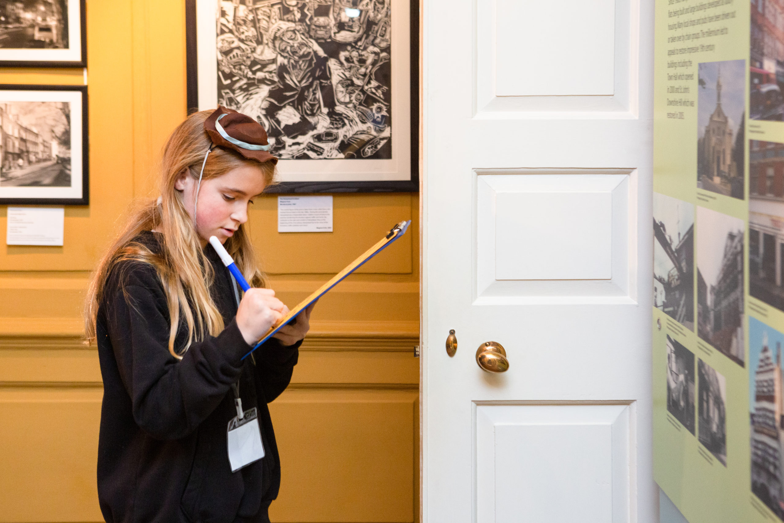 A young girl writes on a clipboard in a gallery at Burgh House.