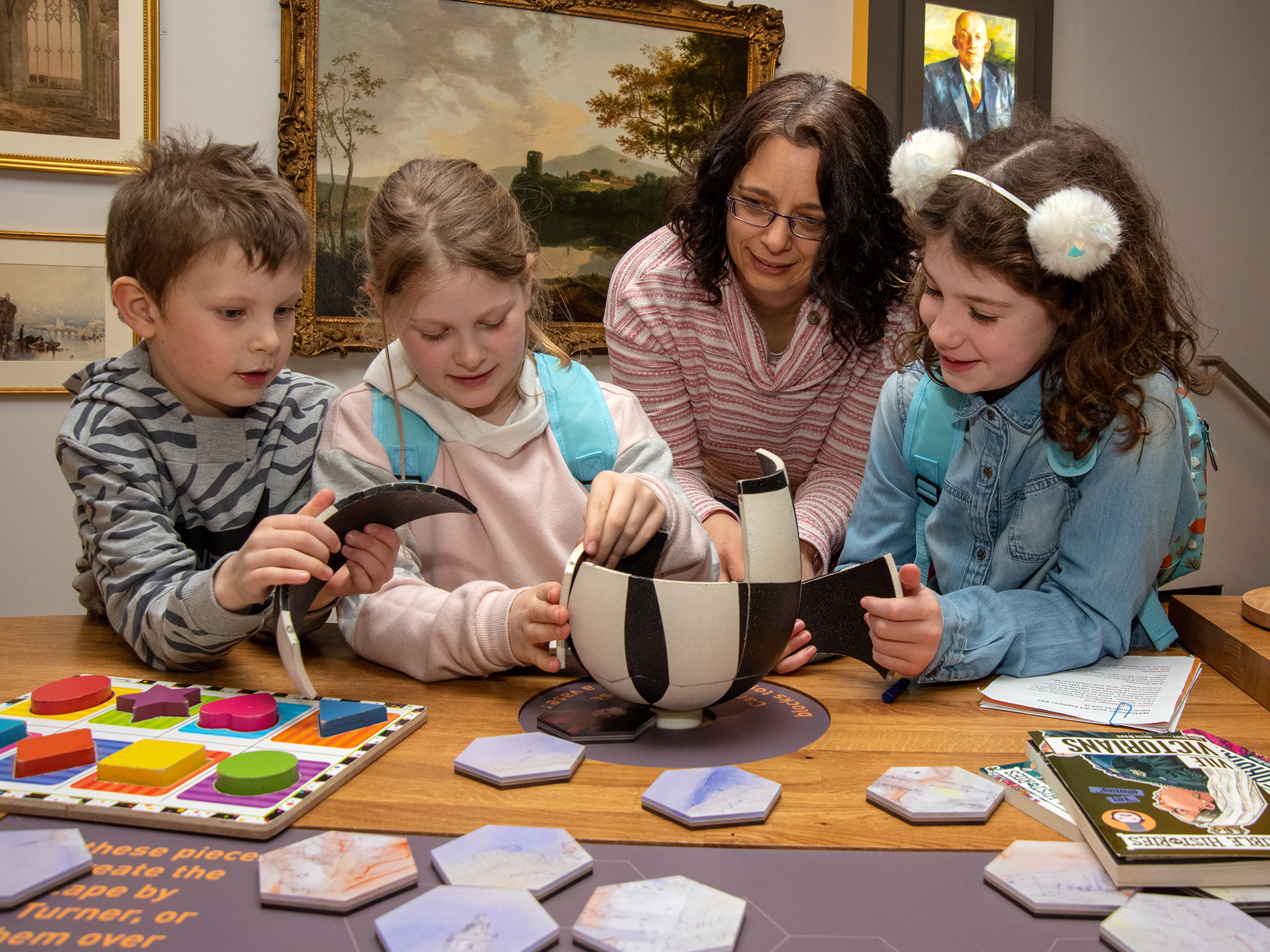 Three children and an adult gather around a table to put together a craft activity in a gallery.