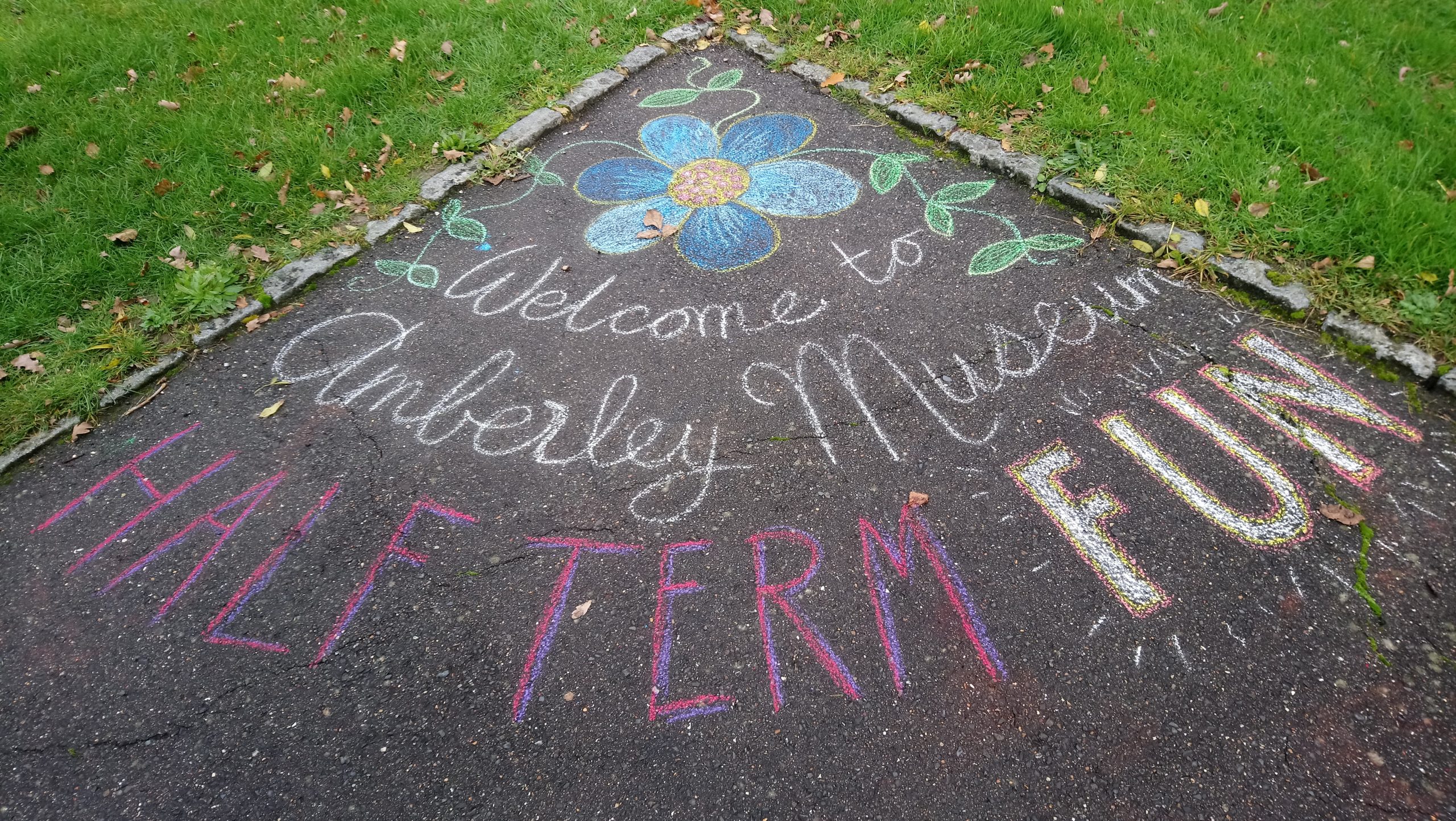 A concrete decorated with the chalk words: Welcome to Amberley Museum Half Term Fun with a blue flower.