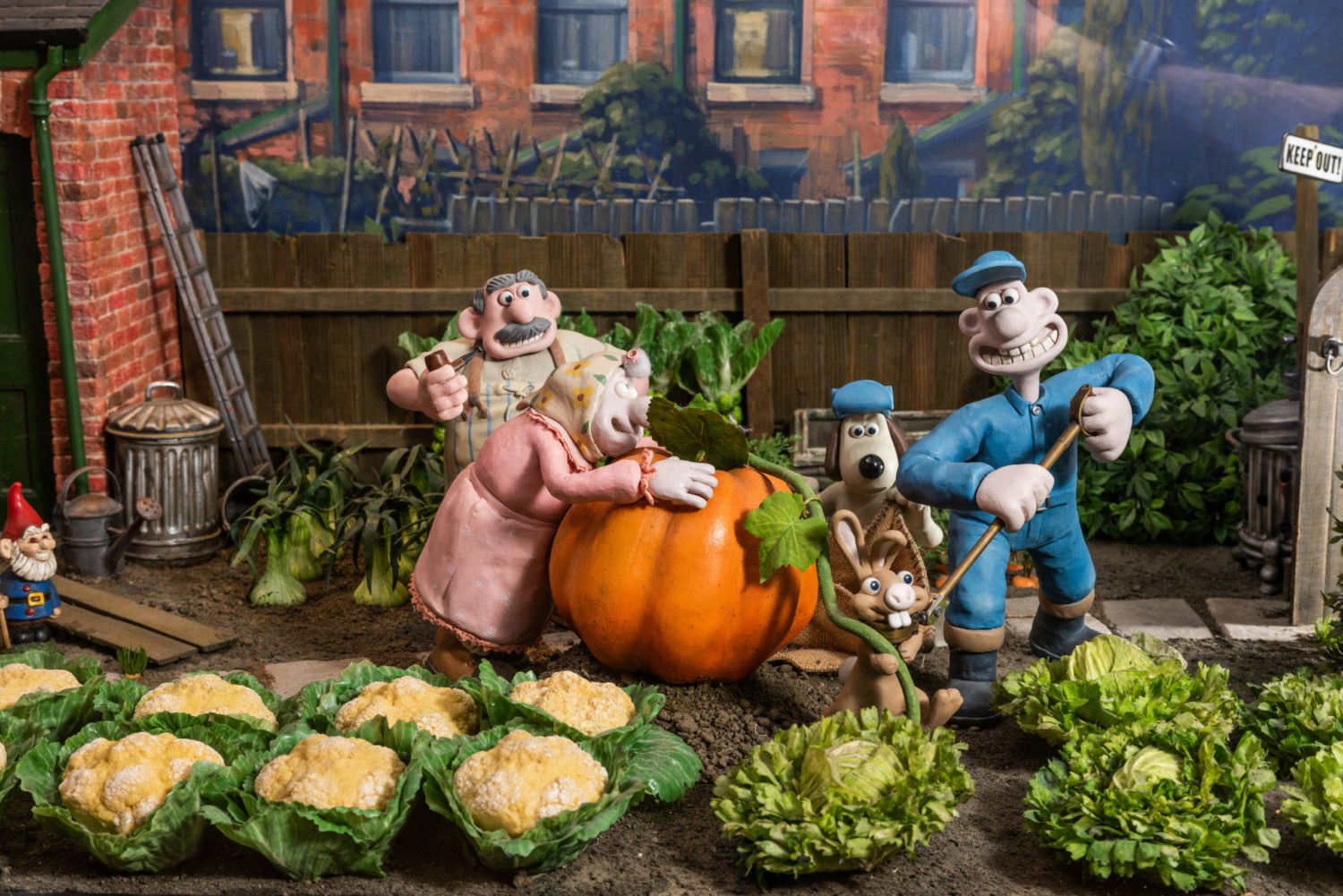 Plasticine models of Wallace, Gromit, an old lady and man and a rabbit digging up a giant pumpkin in a garden.