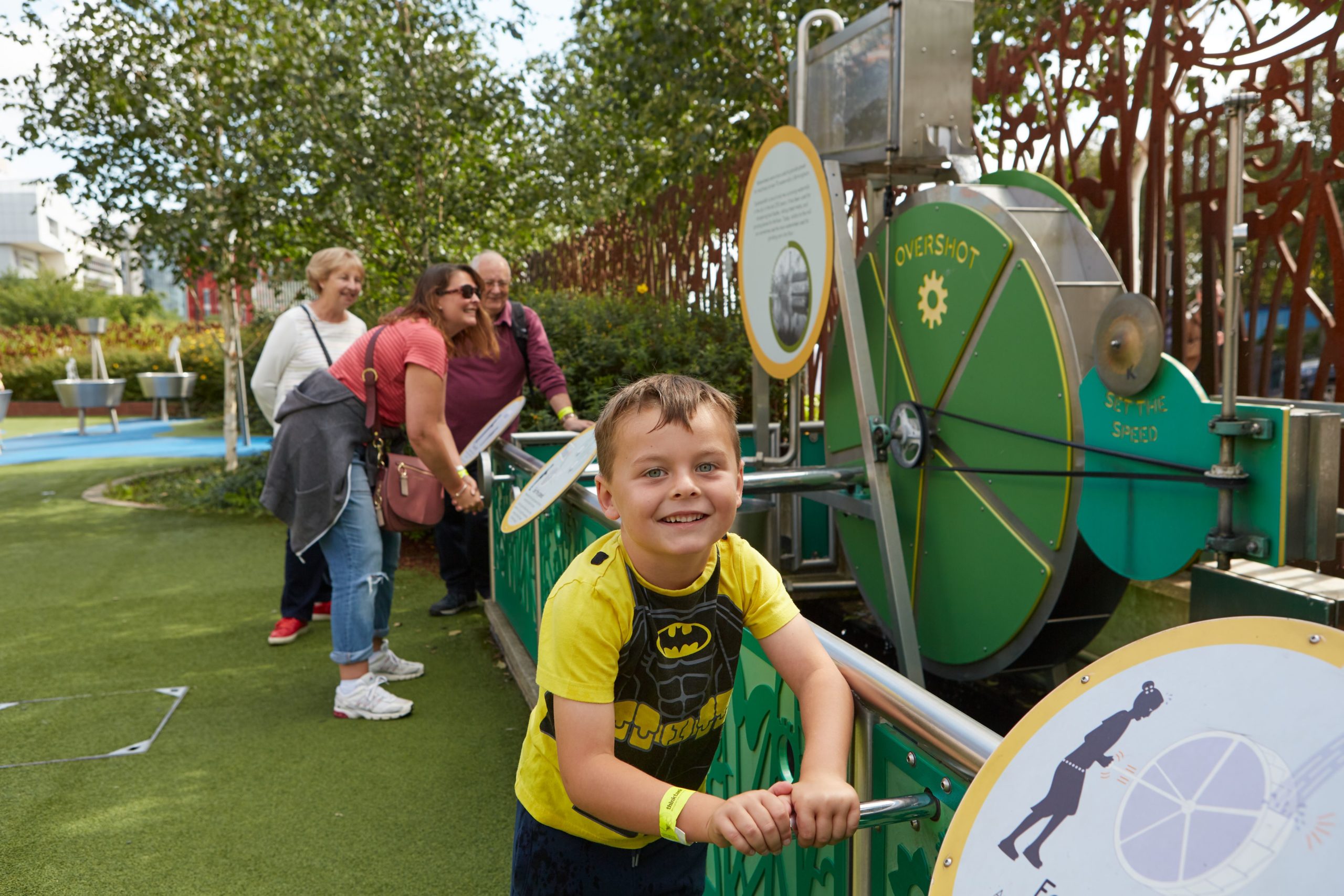 A young boy pulls a lever on a museum interactive outdoors at Thinktank museum. His family pull another handle behind him.