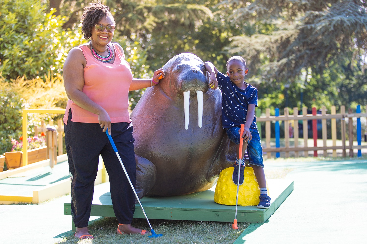 A woman and a young boy stand either side of a walrus statue holding golf clubs.