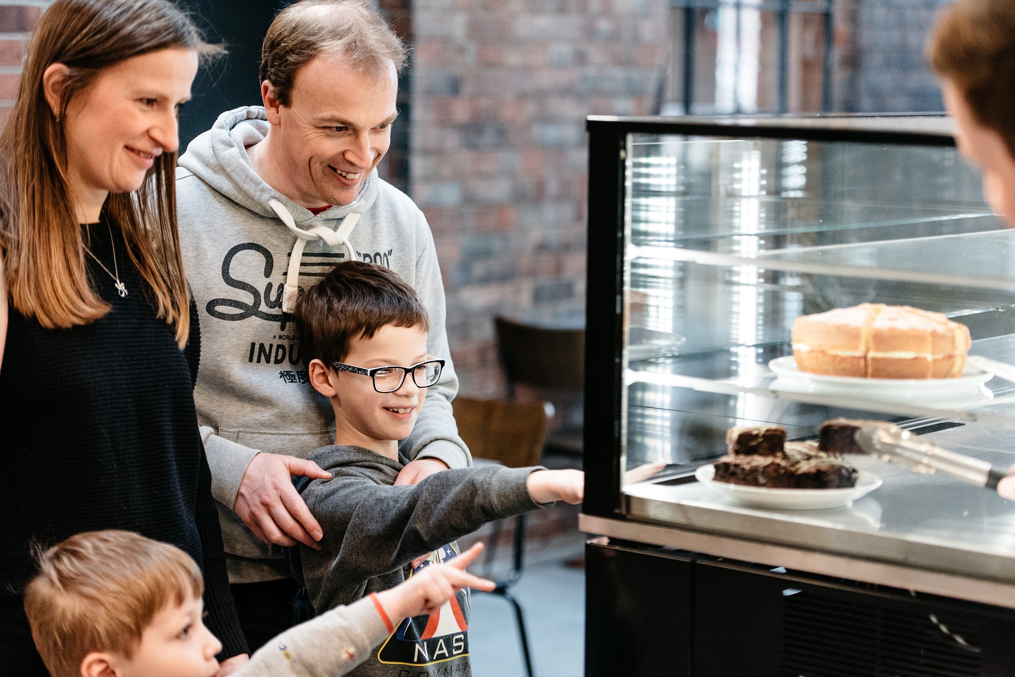 A family stand in front of a cake case at the museum of making with two young boys point at the cake.