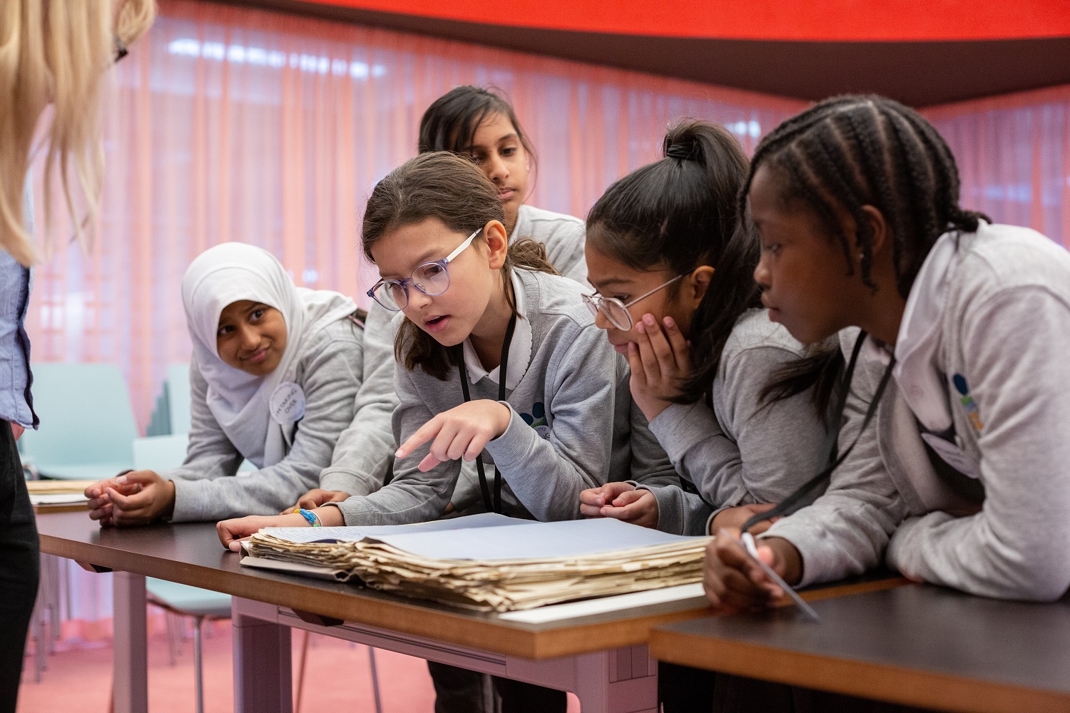Five pupils gather round and examine a large historic book at the National archives.
