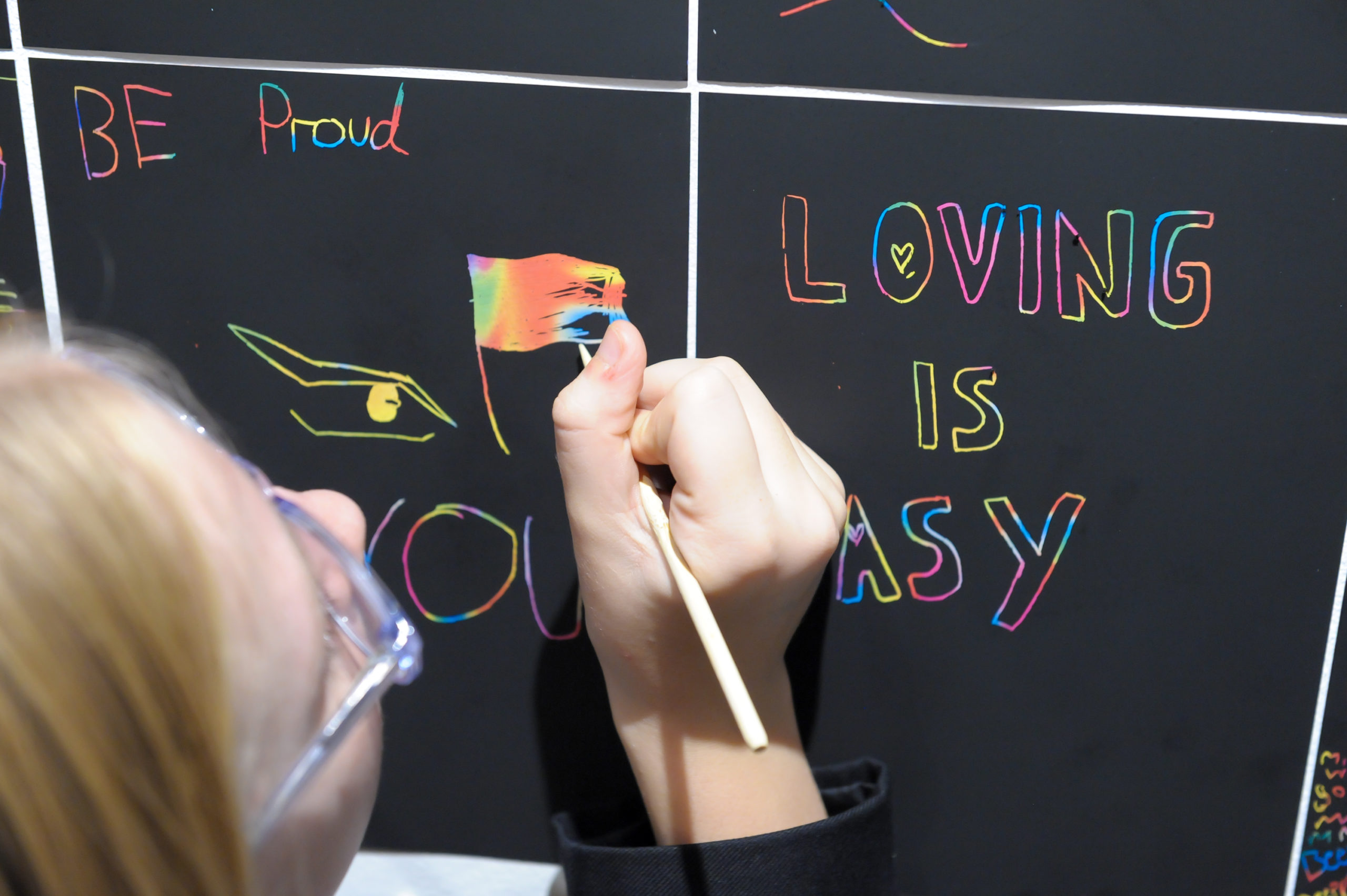 A teen draws a rainbow flag on a chalkboard at the National Justice Museum.