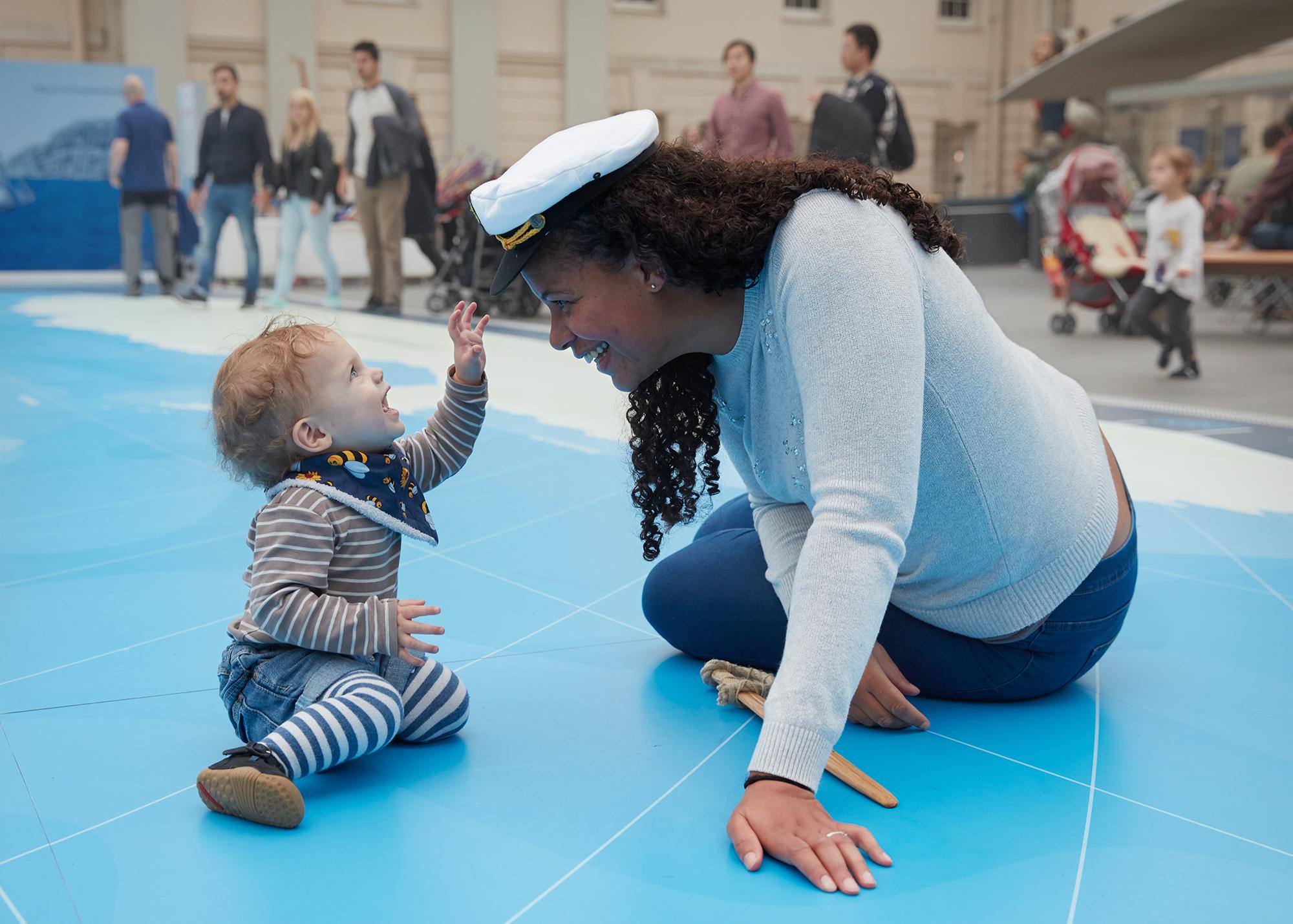 A toddler reaches up to an adult's sailor hat at the National Maritime Museum Ahoy children's gallery.