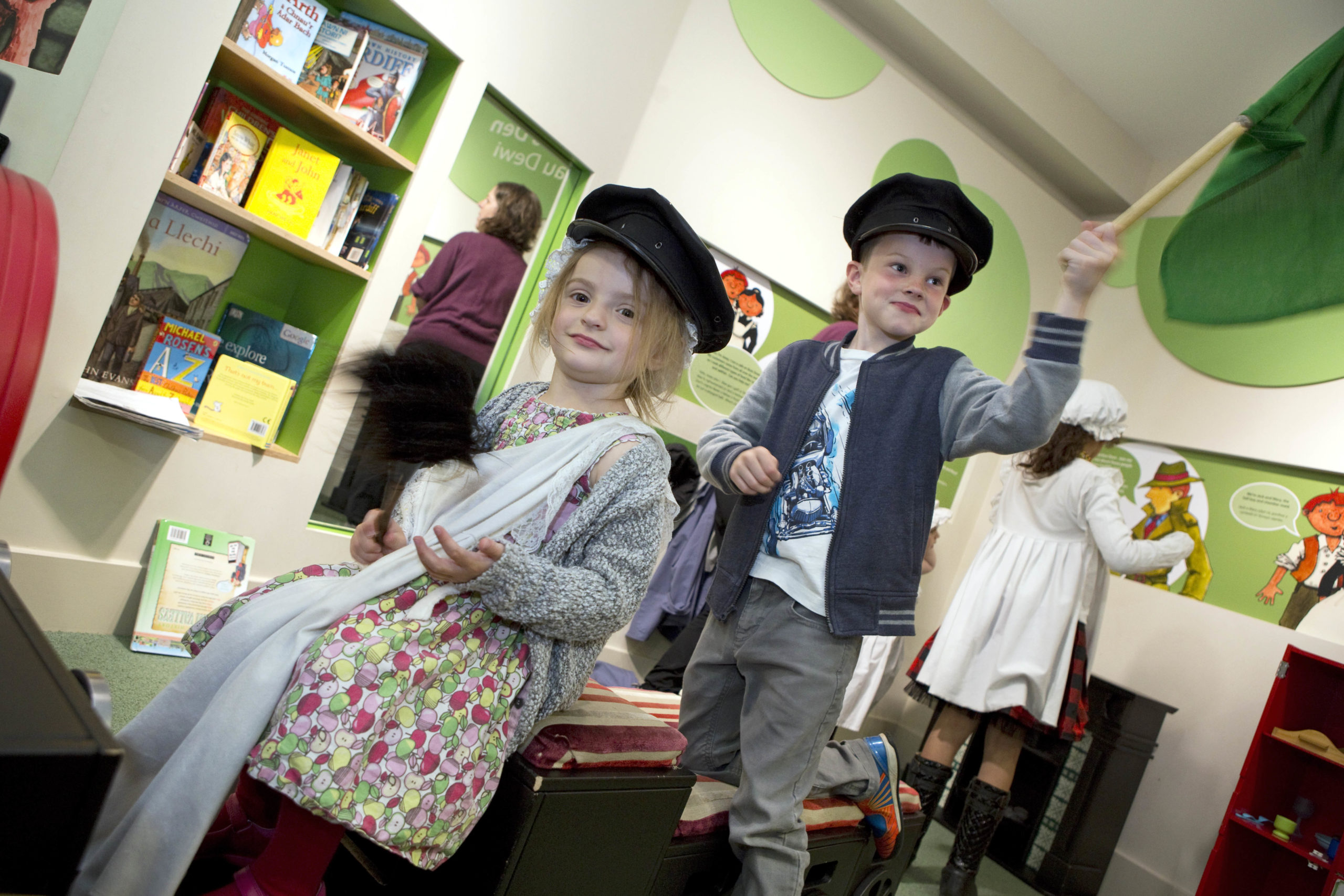 Two children in the Museum of Cardiff wearing hats, one waving a flag and the other a duster.