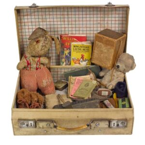 An old fashioned suitcase filled with an assortment of WW2 objects. These include two stuffed toys, some books, an identity card, and an evacuee box.