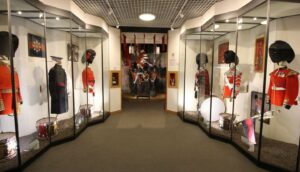 A gallery displaying the uniforms of the King's Guard alongside marching band equipment. The gallery has two display cases on either wall and one at the end of the room.