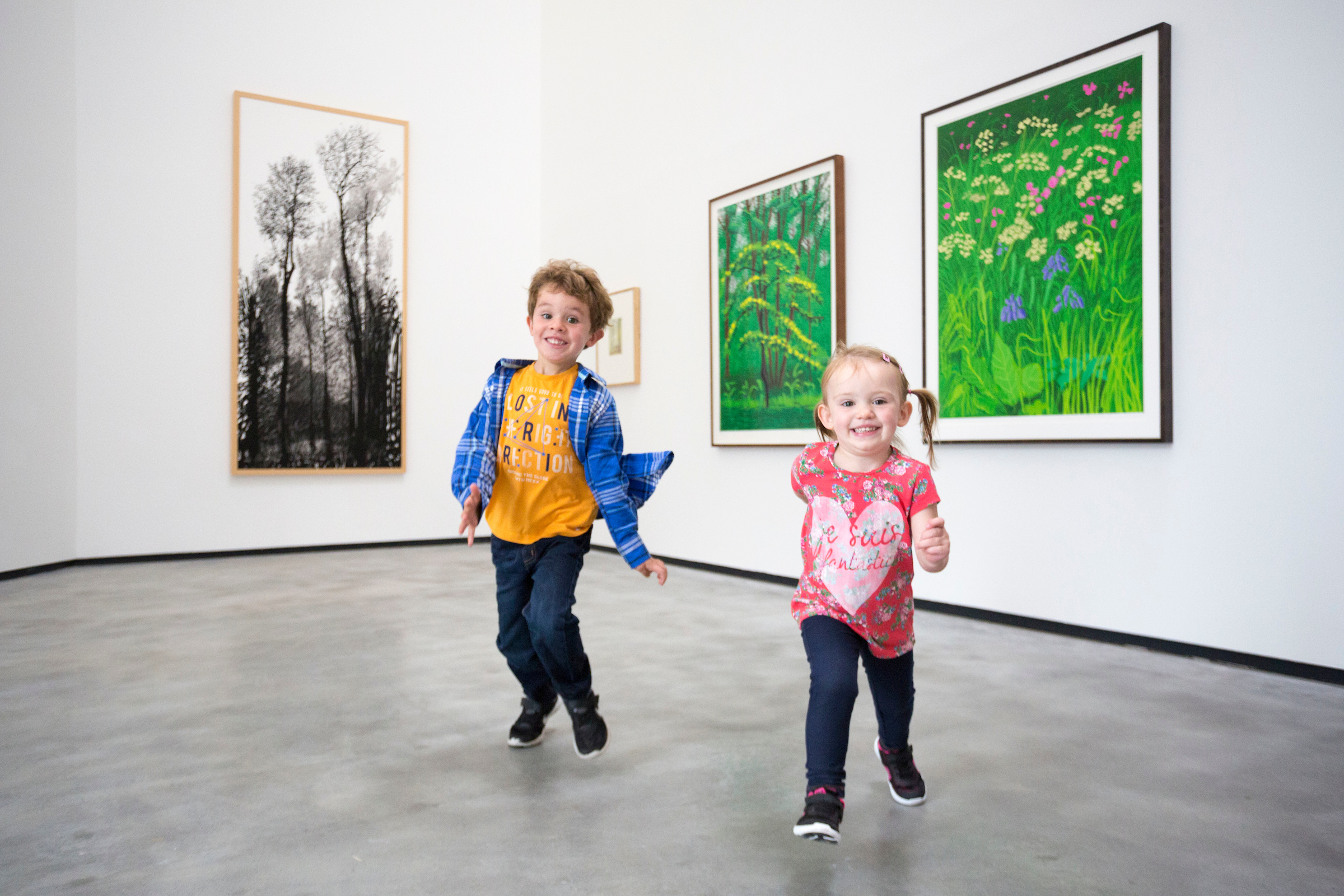 Two small children grinning run through a white gallery at The MAC Belfast.