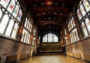 A grand empty hall with stained glass windows and wooden paneling on the ceiling.