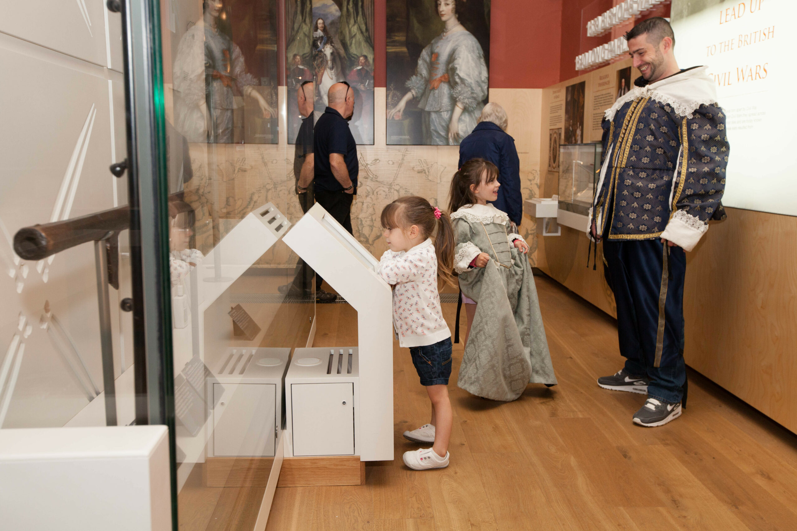 Family visitors in a gallery at the National Civil War Centre. A young girl and an adult are dressed up in historic dress, while a child looks at an interactive screen.