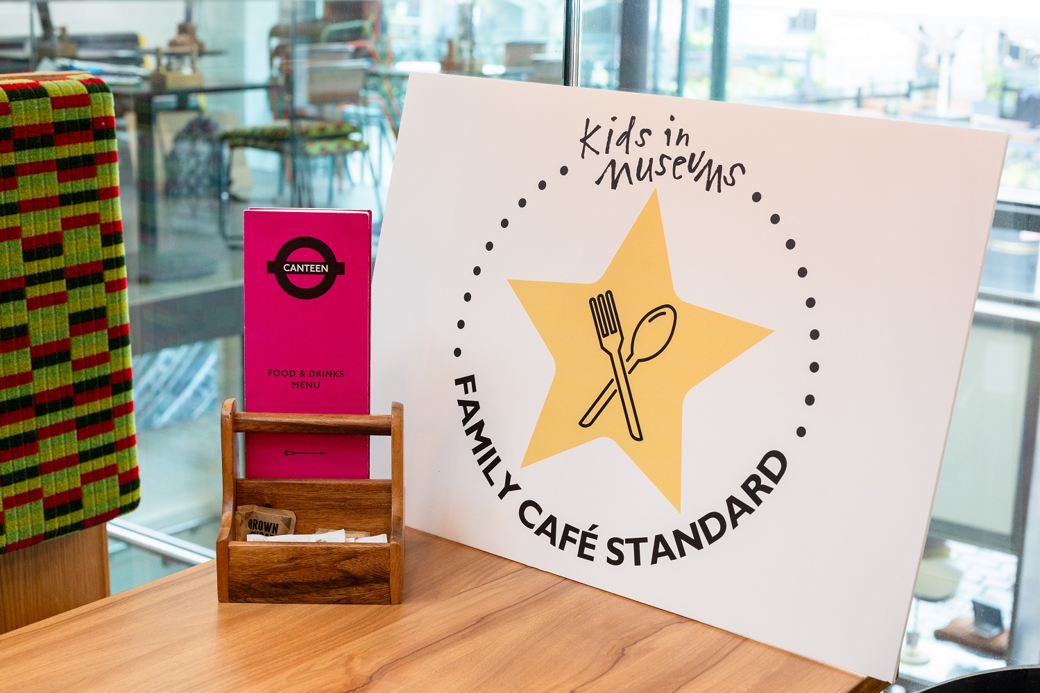 A large sign with the Kids in Museums Family Café Standard logo (a star with a crossed fork and spoon in the middle) stood on a table at Canteen, the London Transport Museum café, one of 20 accredited sites in the UK.