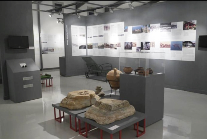 Interior of the museum. Within the room, there are glass cases with a variety of pots and stones. On the wall behind, there are text panels and photographs