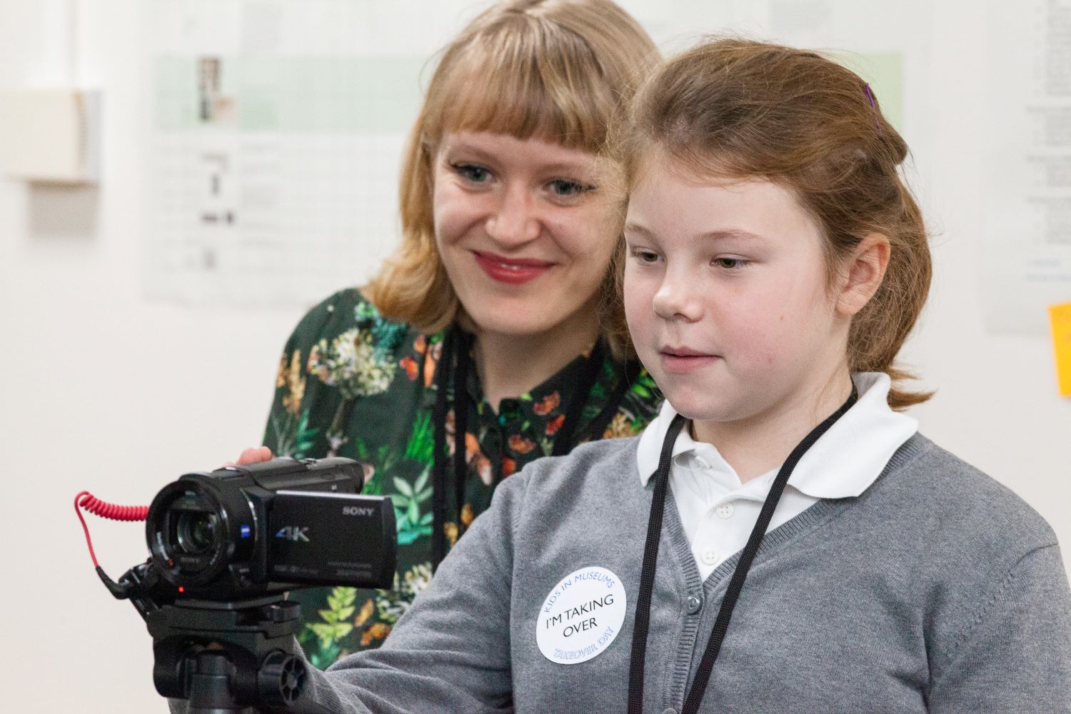 A young schoolgirl looks through a video camera next to a museum staff member.