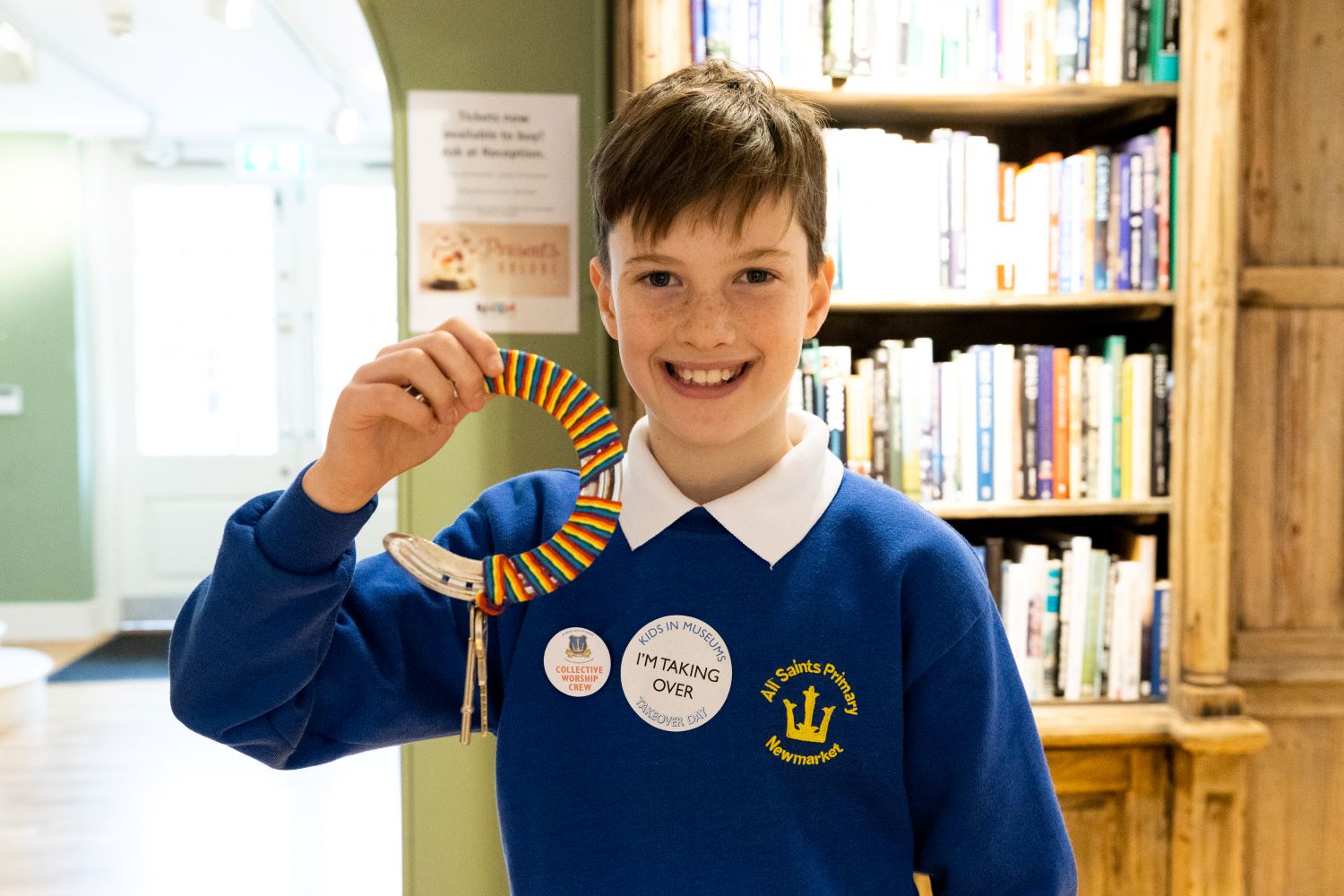 A young boy grins and holds up a set of keys on a circular keyring inside the National Horseracing Museum.