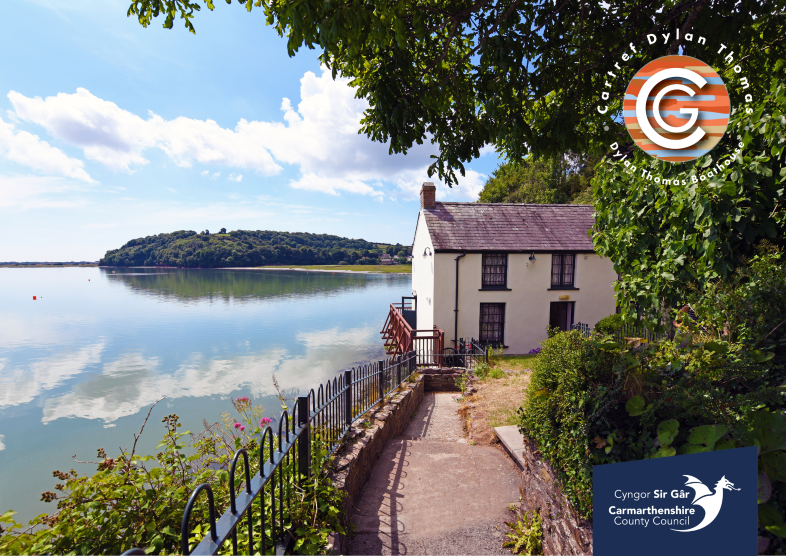 A path leads down to a white house with bushes on the left, and a river on the right. The sky is blue. There are two logos on the photo - one for the Dylan Thomas Boat House and one for Carmarthenshire County Council